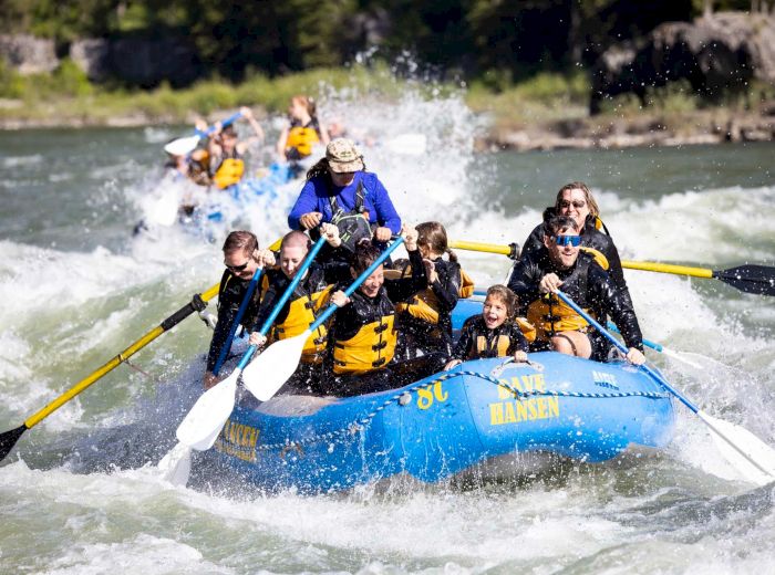 A group of people in life jackets are white-water rafting down a river, experiencing splashes and rapids.